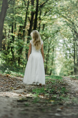 adorable blond girl walking in sunny day in magical forest