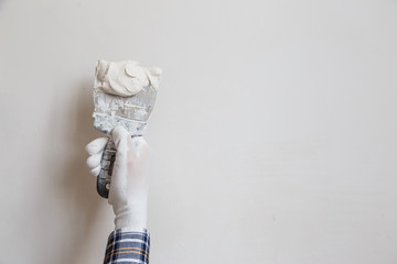 Worker in white gloves performs plastering of the walls of the room.