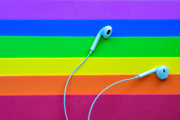 White wired headphones, headset on a multi-colored rainbow background (lgbt). Musical day
