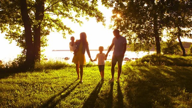 Happy family walking near the sea. Field and trees in countryside. Warm colors of sunset or sunrise. Loving parents and beautiful children. Love and parenthood.