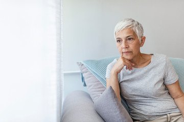 Depressed senior woman near window at home. Lonely senior woman. Pensive woman. Sad Mature Woman...