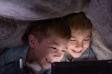 Brothers kids boys watch tablet computer under blanket