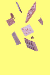 Levitating pieces of broken chocolate on a yellow background..