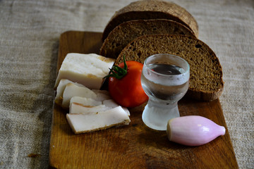  Freshly baked bread on a wooden cutting board with bacon, tomato, onion and a shot of vodka