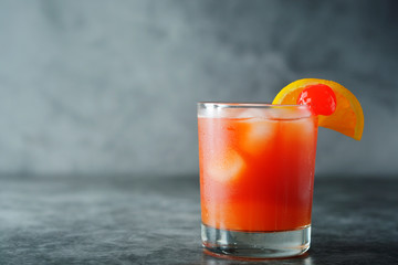 Summer cocktail. Orange juice with mint, syrop, fruit slices and cherry with ice. Dark background.