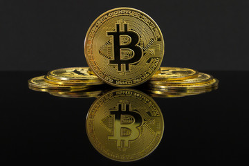 A mirror reflection of a big golden BTC coin. The coin of bitcoin is on a black table and black...
