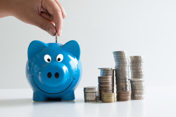 hand putting coin in blue piggy with coins pile