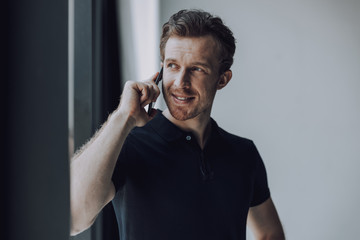 Man in black polo shirt talking on the phone and smiling - obrazy, fototapety, plakaty