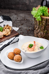 Cream soup with shrimps in white plate and plate with cheese balls on dark concrete background