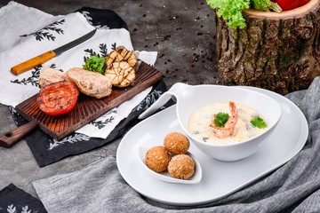 Cream soup with shrimps in white plate and plate with cheese balls on dark concrete background