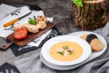 Cream soup with salmon in a white plate on dark concrete background