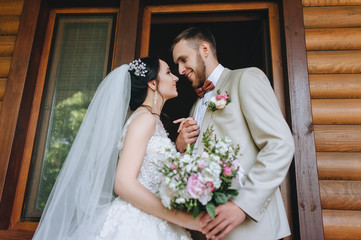 Beautiful newlyweds hugging and smiling against the background of a wooden house. Wedding portrait...