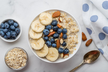 Oatmeal porridge with blueberries, almonds and banana on marble table - obrazy, fototapety, plakaty