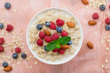 Oatmeal with raspberries, almonds and blueberries and mint  on pink background