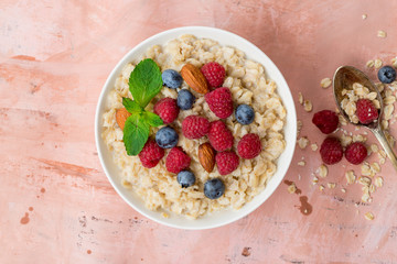 Oatmeal with raspberries, almonds and blueberries and mint  on pink background