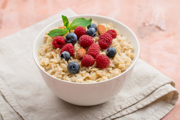 Oatmeal with raspberries, almonds and blueberries and mint  on pink background