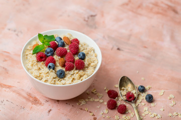Oatmeal with raspberries, almonds and blueberries and mint  on pink background