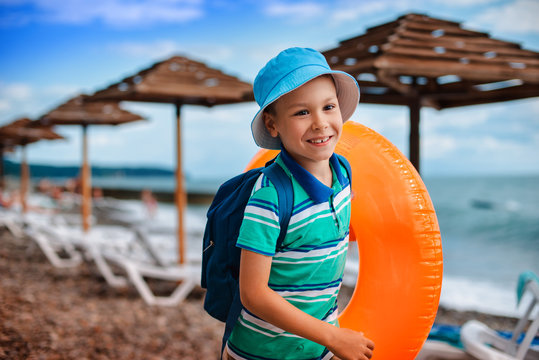 little Boy 6 years old in a hat with an inflatable orange circle runs along the beach during the summer holidays.