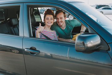 Cheerful young woman sitting in the car with friend and showing thumbs up
