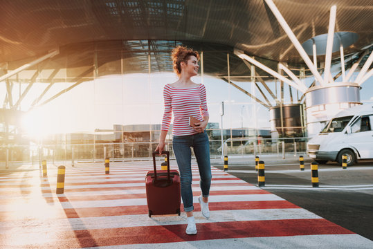 Beautiful young woman with travel suitcase crossing the road in airport