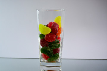 Multicolored tasty candies in a glass cup on the mirror. The reflection of the glass and sweets creates a striking effect of volume and increases the number of objects in the frame, which makes sweets