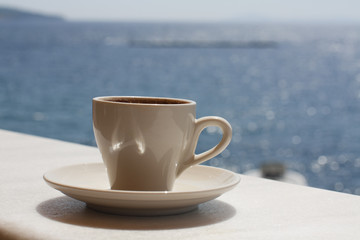 White cup with coffee on the background of the sea. Sunny day, vacation at sea. Enjoyment moment. Enjoying a cup of coffee by the sea.