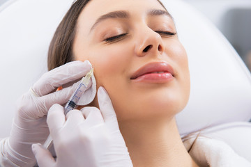 Young lady on procedure of cheek zone in salon