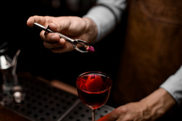 Bartender putting a little rose bud to the red cocktail in the glass