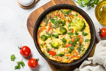 Frittata with vegetables on white stone table.