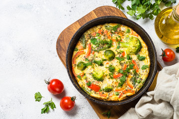 Frittata with vegetables on white stone table.