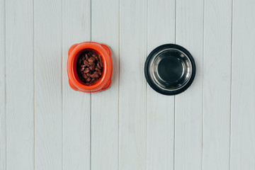top view of bowl with pet food and empty bowl on wooden surface with copy space