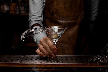 Professional male bartender mixing a transparent alcoholic drink in the martini glass with one olive