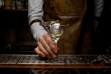 Bartender mixing a transparent alcoholic drink in the martini glass with one olive
