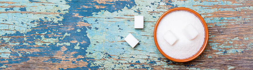 Sugar granulated and refined sugar in a bowl on a wooden table. Top view. Web banner