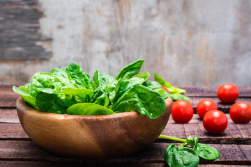 Fresh baby spinach leaves in a bowl and cherry tomatoes on a wooden table