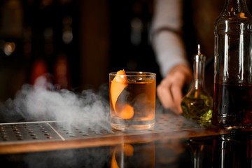 Golden cocktail in the glass with one big ice cube and orange zest