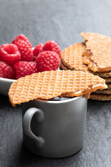 Melted Dutch caramel waffles with cup of coffee and fresh raspberry on black stone background