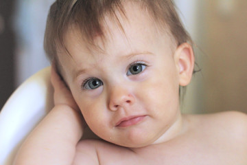 Close-up portrait of a cute smiling little white baby sitting in a chair without clothes