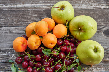 Close up picture of orange riped peaches, green apples, red gooseberries and sour cherries just after harvest on old wooden table in the garden. Summer seasonal fruits full of nutrients and vitamins.