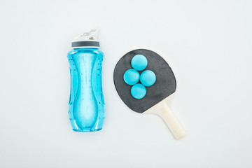 top view of blue sport bottle near ping pong balls and rackets isolated on white