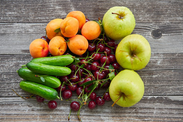 Freshly harvested summer seasonal organic fruits and vegetables from small home garden on the vintage wooden table consist from cucumbers, green apples, apricots and sour cherries. Raw vegan diet food