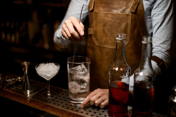 Professional bartender stirring an alcoholic drink with ice in the measuring glass cup