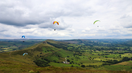 Group of paragliders flying above valley with green mountain and clouds in the background
