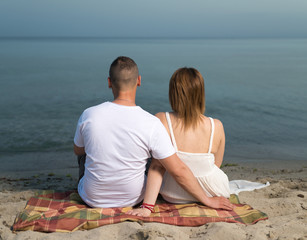 Young couple in love relaxing on beach, sitting on the sand.