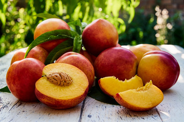 Ripe peaches with leaves on the old wooden table against the background of green leaves. Fresh...