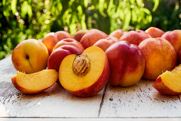 Ripe peaches with leaves on the old wooden table against the background of green leaves. Fresh sweet sliced peaches in the garden. Soft selective focus