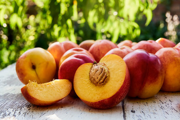 Ripe peaches with leaves on the old wooden table against the background of green leaves. Fresh sweet sliced peaches in the garden. Soft selective focus