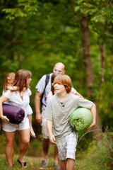 Fototapeta premium Family with three children (6-7, 12-13, 16-17) walking through woods with camping gear
