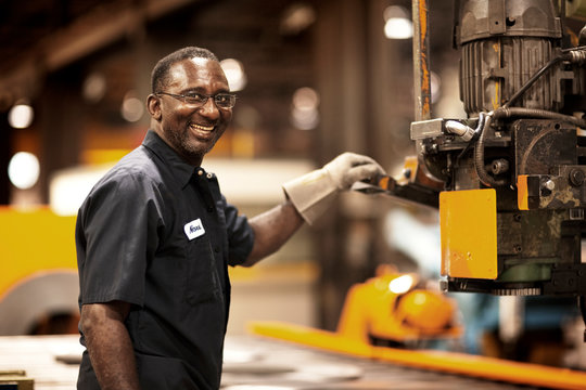 Smiling mature worker using machinery in factory