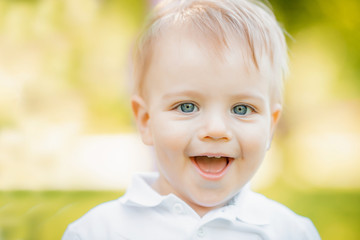 Portrait little baby boy looking into frame and smiling, walking in park